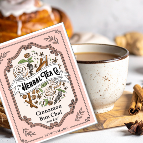 Herbal Tea Co. Cinnamon Bun Chai packaging with a cup of tea and cinnamon sticks on a wooden board.