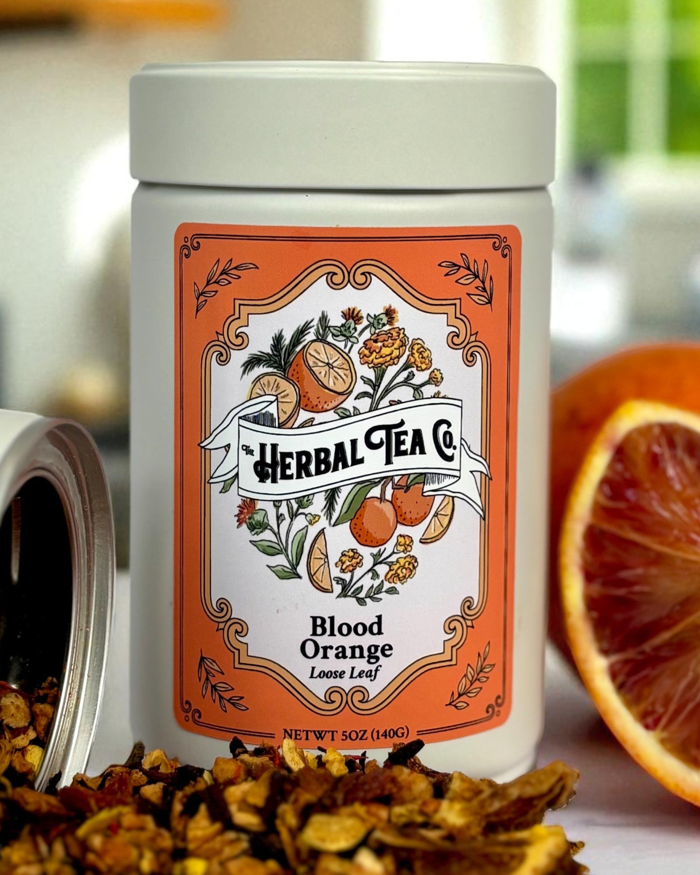 Herbal Tea Co. Blood Orange tea canister with dried herbs on a kitchen counter.
