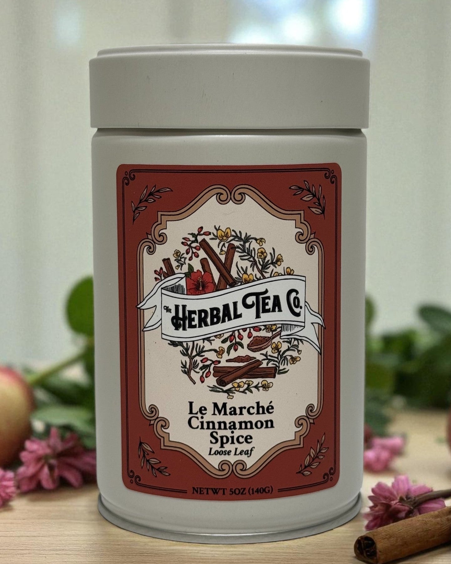 Herbal tea canister with decorative label on a wooden surface with cinnamon sticks and apples.