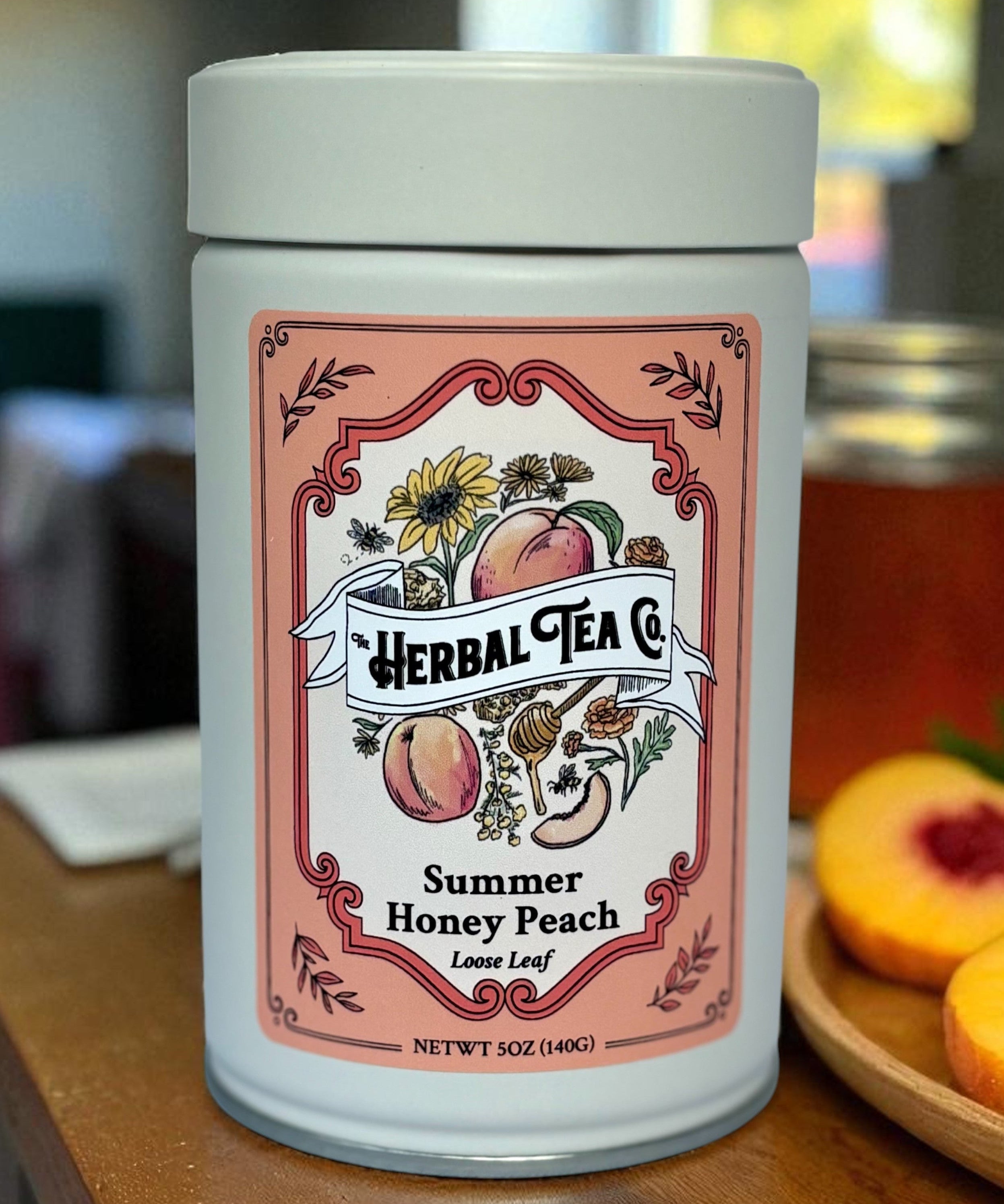 Herbal Tea Co. Summer Honey Peach tea canister on a wooden surface with peaches and a blurred background.