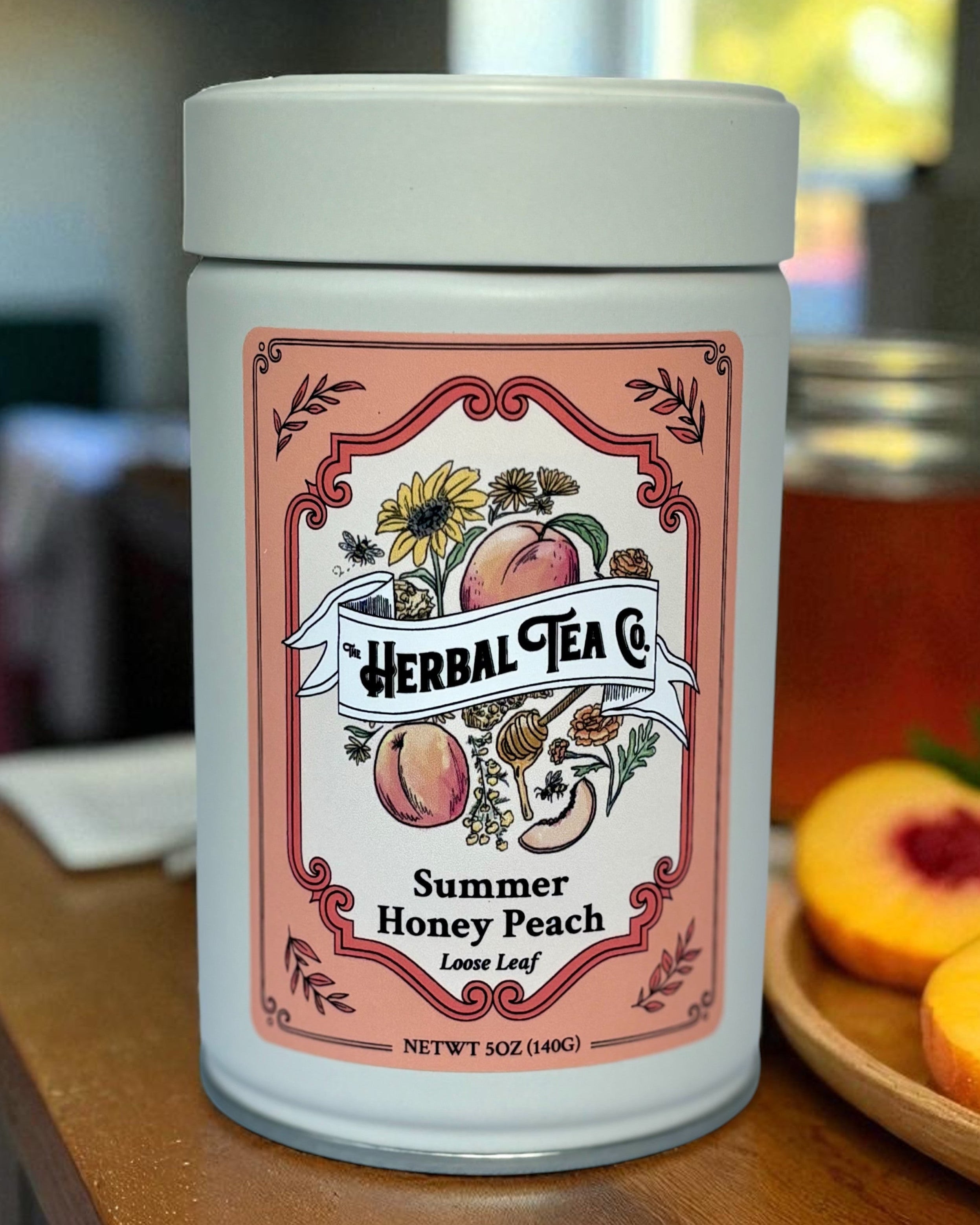 Herbal Tea Co. Summer Honey Peach tea canister on a wooden surface with peaches and a blurred background.