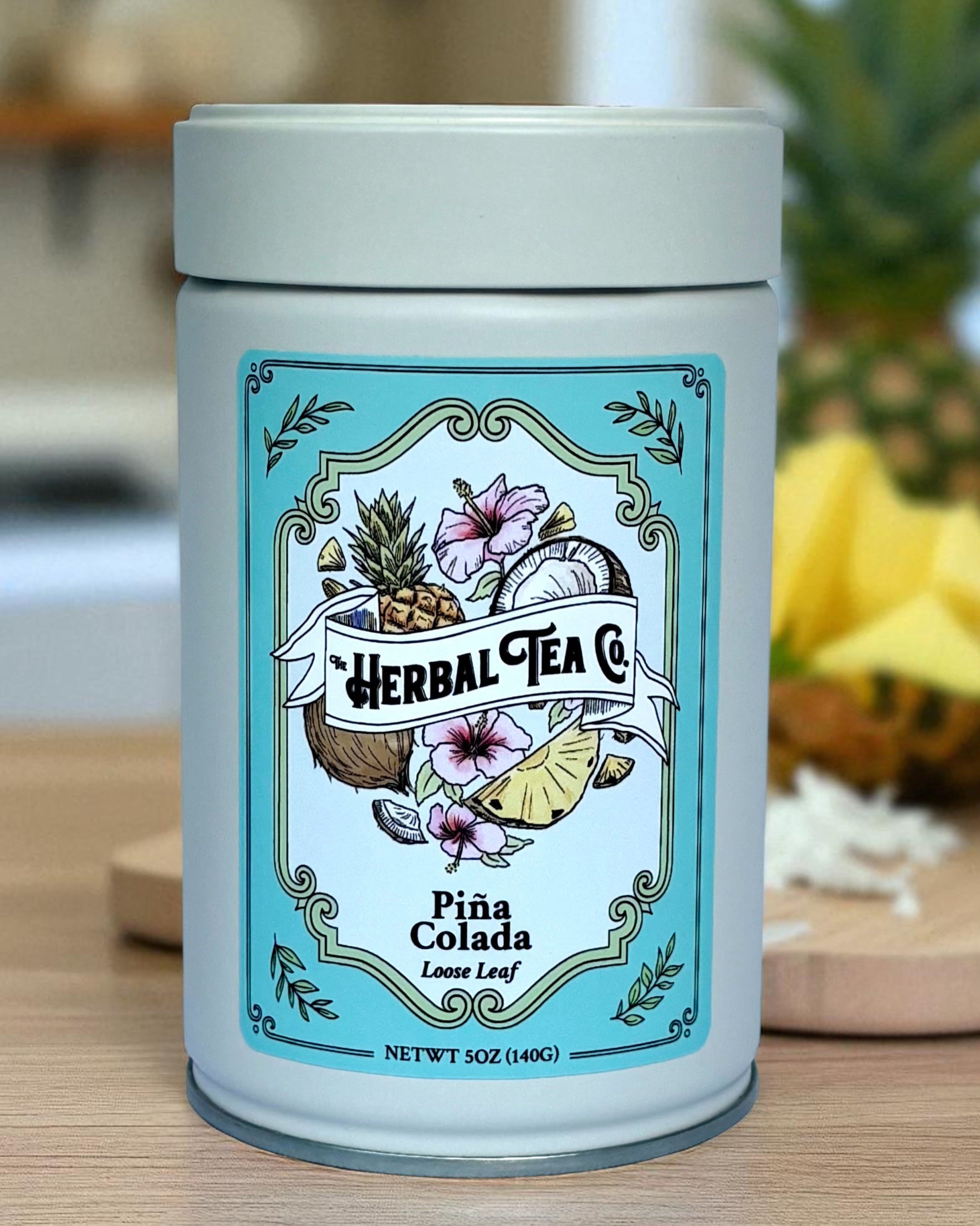 Herbal Tea Co. Piña Colada tea canister on a wooden surface with blurred background