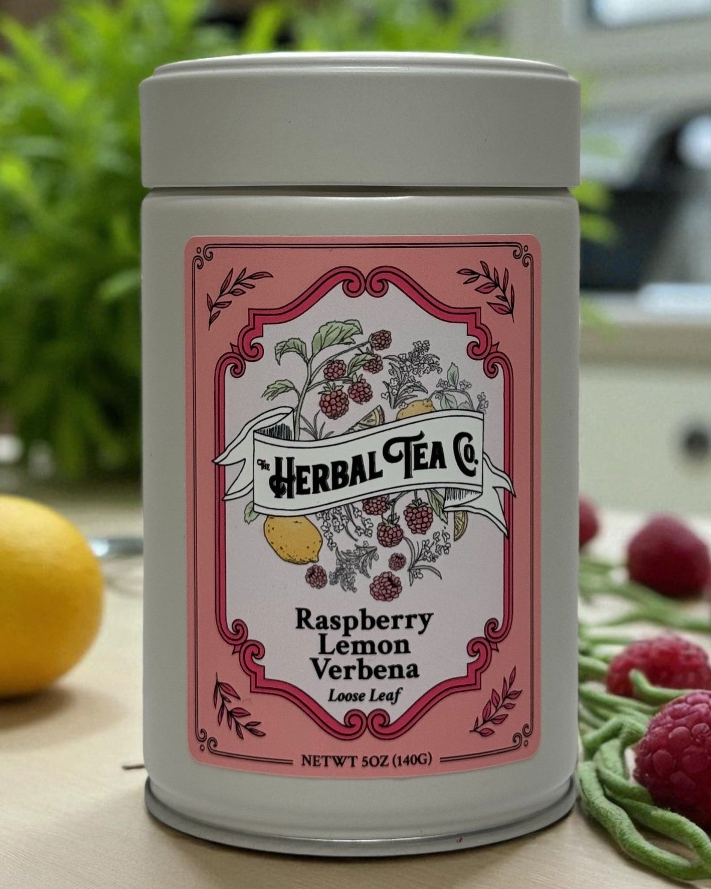Herbal tea canister with pink label featuring illustrations of herbs and fruits on a kitchen counter.