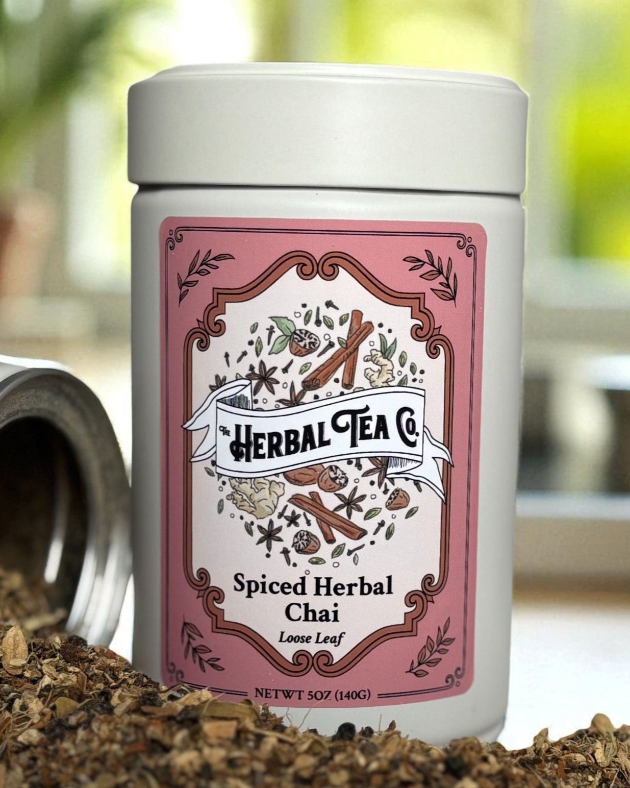 Herbal Tea Co. Spiced Herbal Chai tea canister with a pink label on a blurred kitchen background.
