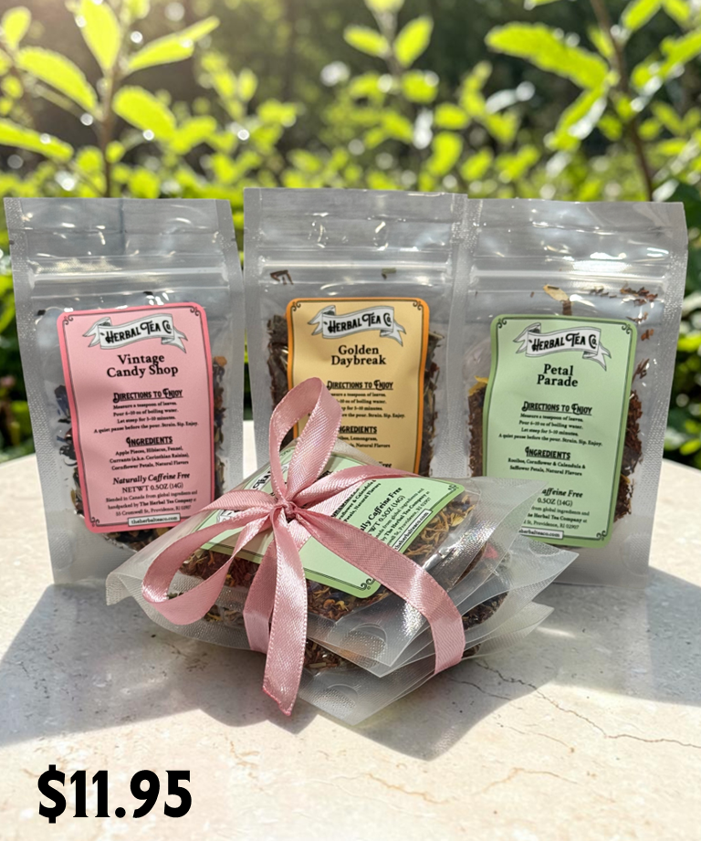 Three tea packages with labels and a pink ribbon on a light surface with greenery in the background.