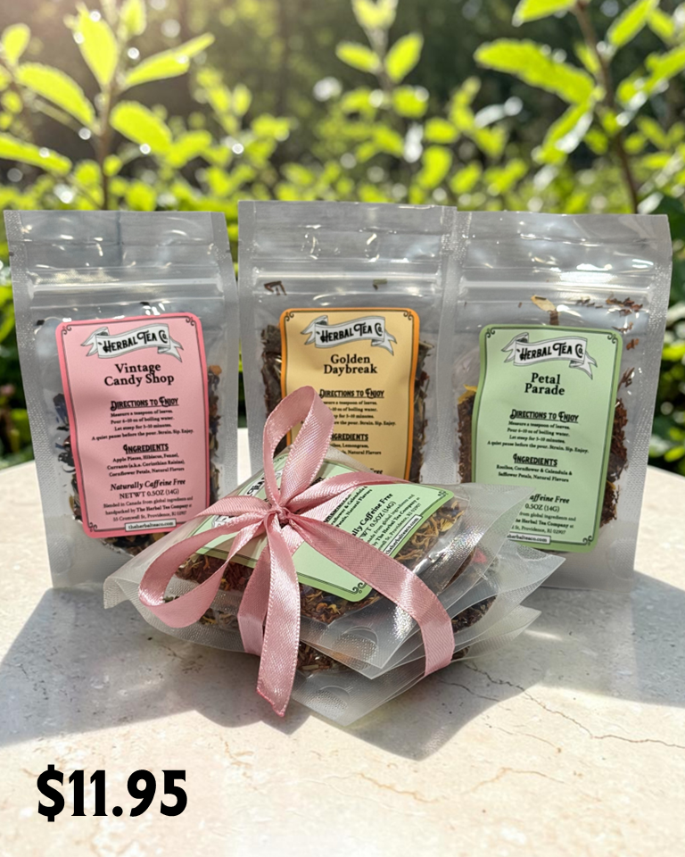 Three tea packages with labels and a pink ribbon on a light surface with greenery in the background.